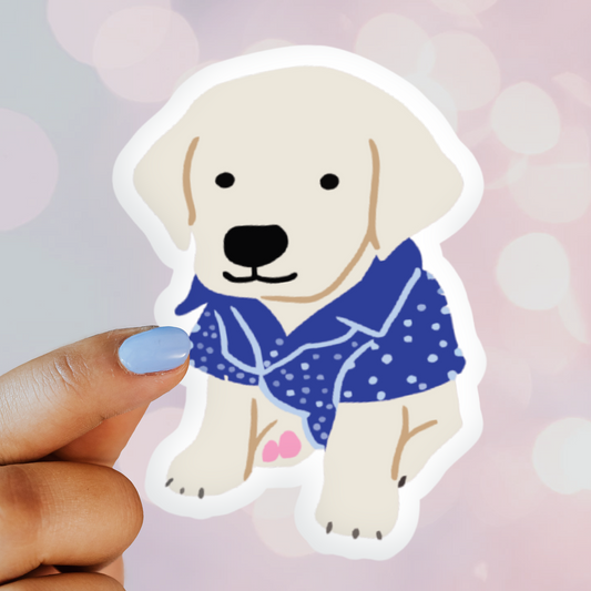 Sticker of a dog wearing a blue outfit held by a hand against a pink background
